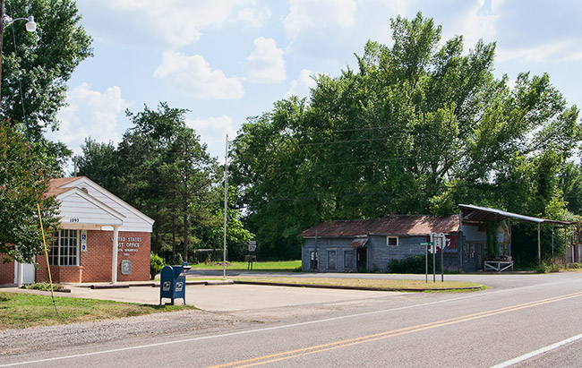 Single-story brick building with parking lot and abandoned wooden building on street with parking lot