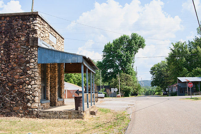 Stone store front with covered porch on street with various building in the background