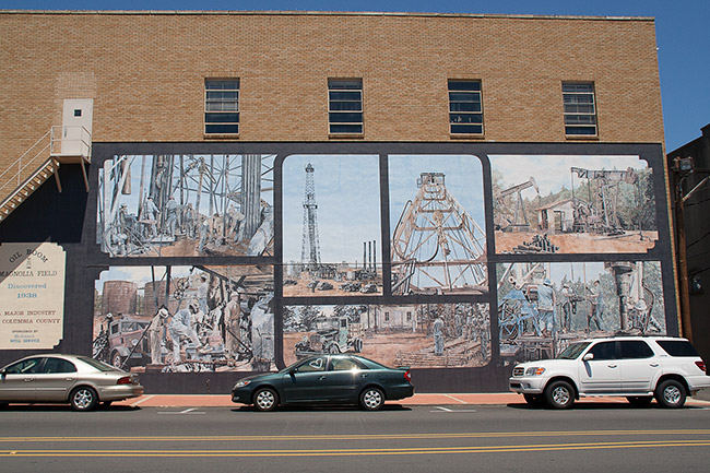 Oil field workers and derricks in mural on side of multistory building on street with parked cars