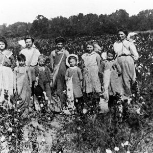 White man women and children standing in cotton field with bags over their shoulders