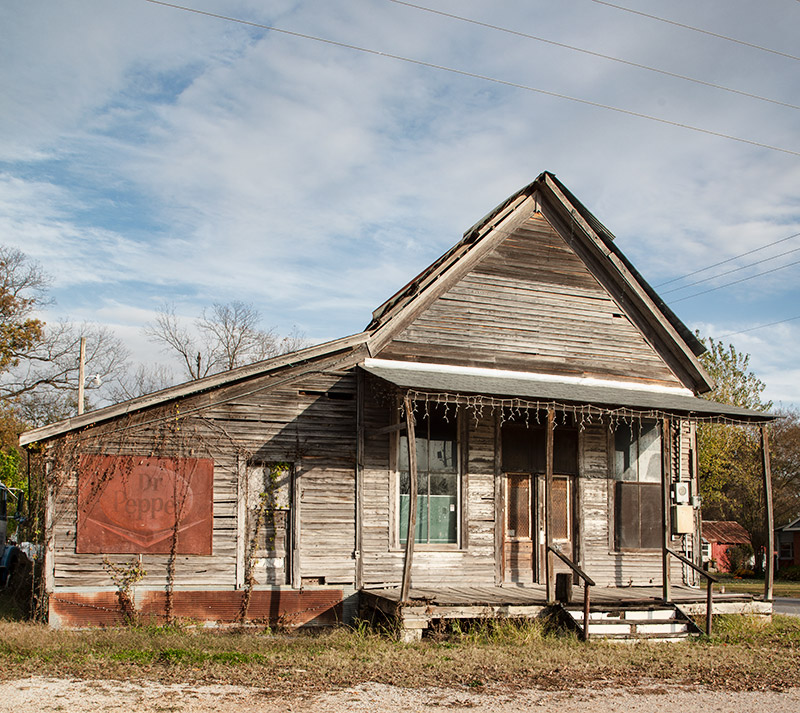 Abandoned building with covered porch and wood siding on grass