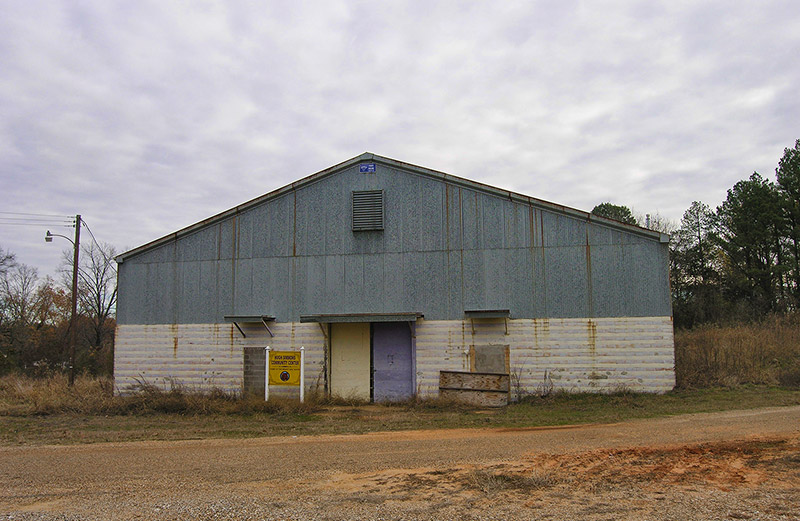 Weathered gray and white building and sign on dirt road