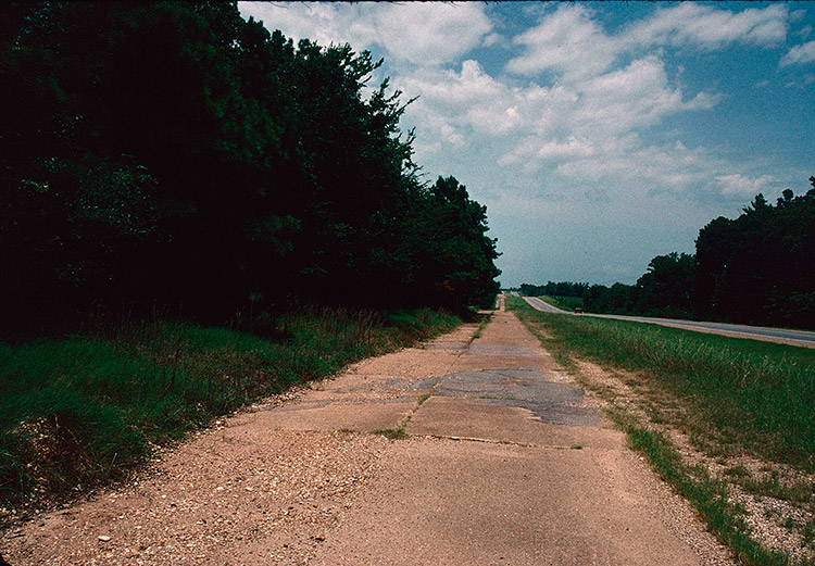 Section of old and crumbling highway with newer road parallel to it