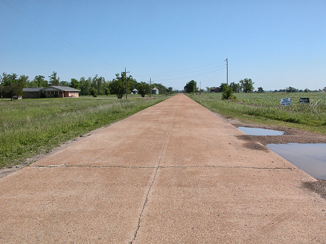 Cracked rural highway with single-story house and silos in the distance