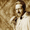 Portrait photo of white man with serious expression pompadour mustache jacket painters palette and long handled brush