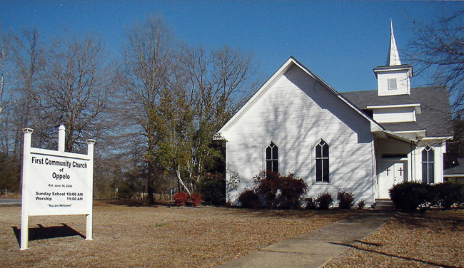 Single-story white church with steeple in autumn with sidewalk and sign