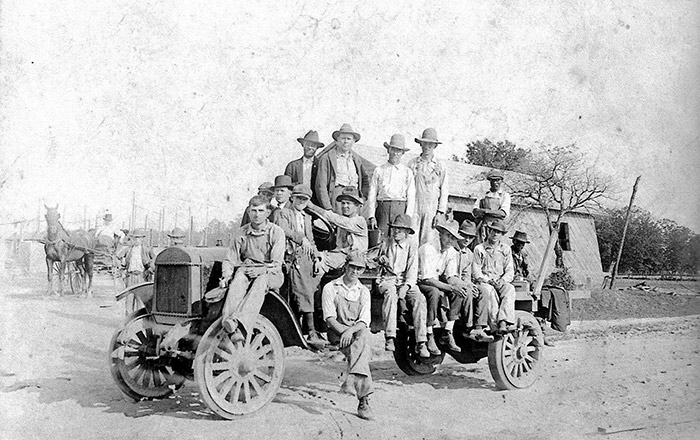 Group of white men sitting and standing on car on dirt road