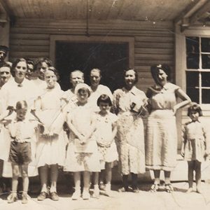 White men women and children standing outside building with covered porch