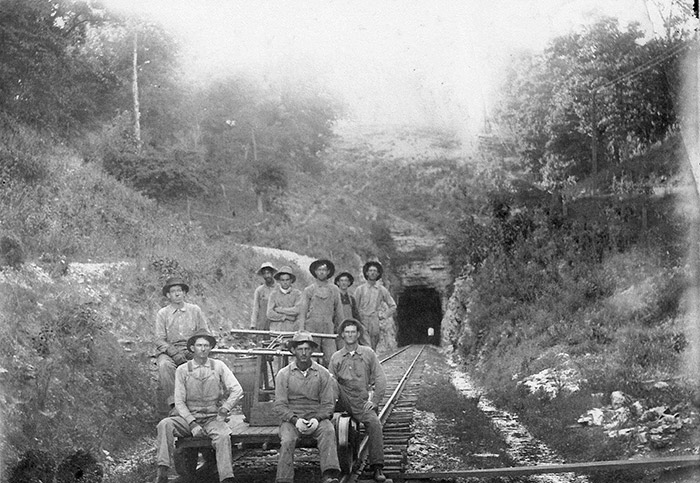 Group of white men on rail cart with hillside tunnel behind them