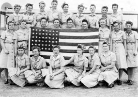 White women in uniform wearing bandanas pose with an American flag