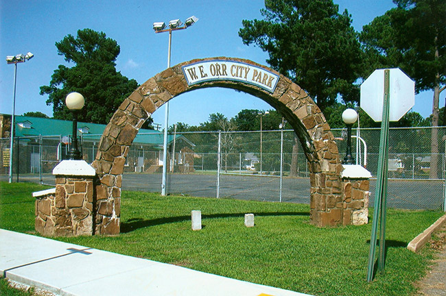 Stone arch entrance at park with basketball court and building with rock walls and street lights