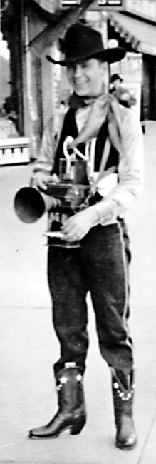Young white smiling man standing in cowboy hat vest rhinestone boots with conical lens camera
