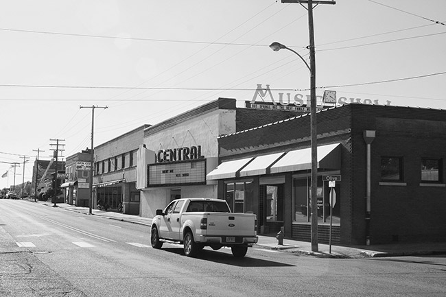 Truck driving by theater and storefront buildings on two-lane road
