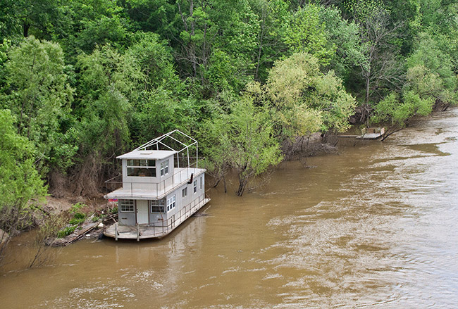 Houseboat on muddy river with trees in the background