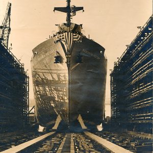 Large ship leaving dry dock with flag banner draped on its bow