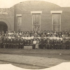 Assemblage of white people in front of brick building
