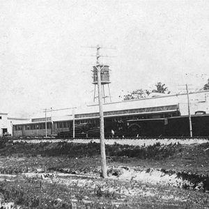 Two long industrial buildings with train on tracks running beside them and telephone poles in the foreground