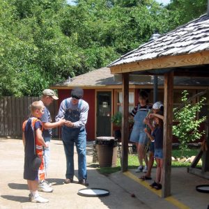 White man in overalls teaching white children to spin tops