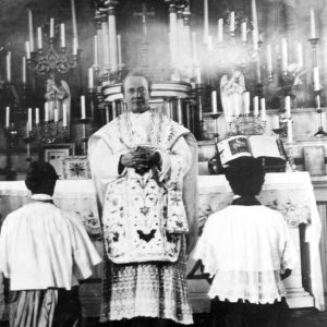 White man in robes in a church with altar boys in their uniforms