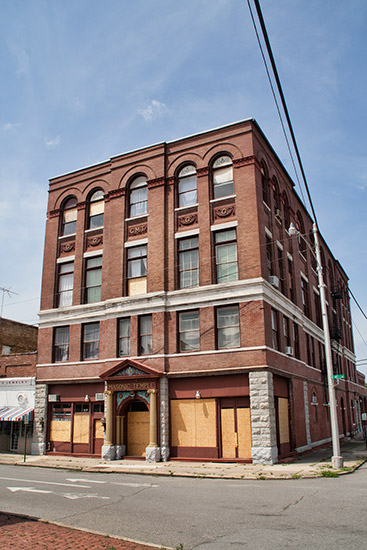 Four-story brick building on street corner with first floor windows papered over