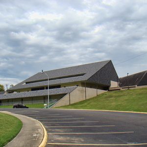 Concrete building with triangular roof on hill side with parking lot