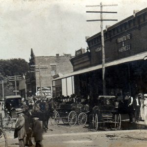 Street scene with storefronts, horses, people, and cars