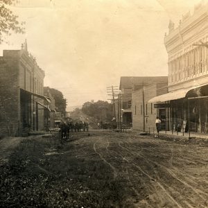 Dirt road lined with storefronts with people and horses