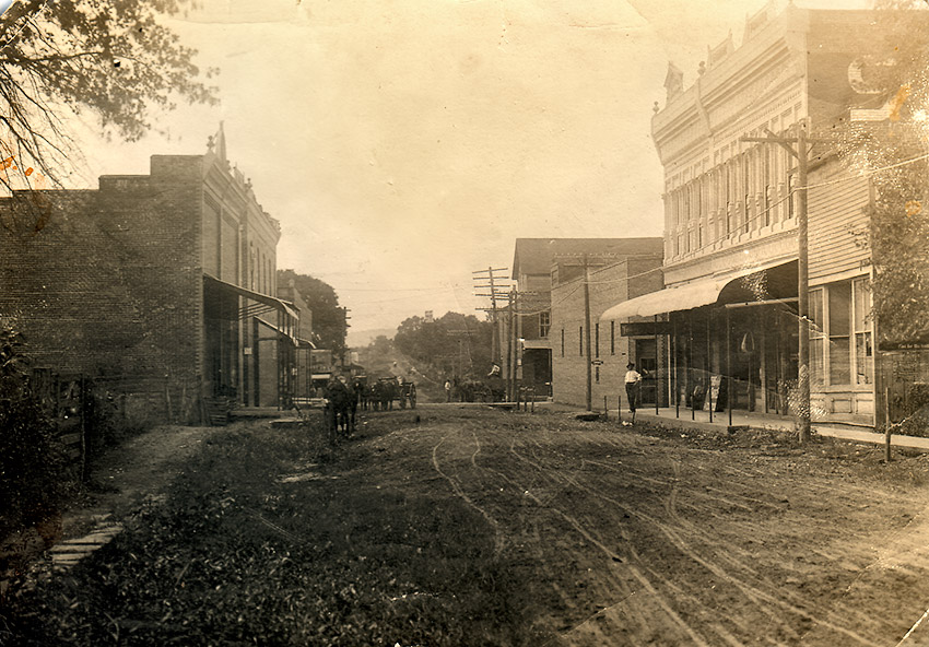 Dirt road lined with storefronts with people and horses
