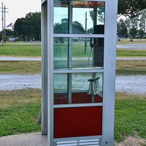 Telephone booth on concrete base with gravel roads behind it