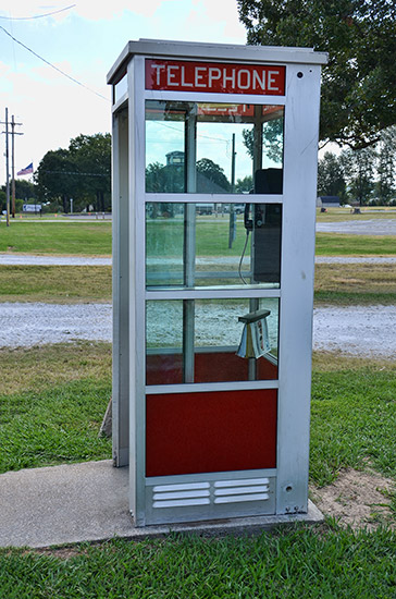 Telephone booth on concrete base with gravel roads behind it