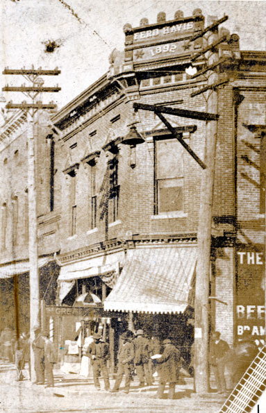 Crowd of men in hats in front of two-story building