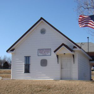 Small white building labeled "United States Post Office" with white siding and flag pole