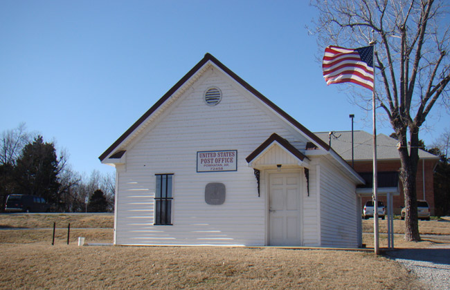 Small white building labeled "United States Post Office" with white siding and flag pole