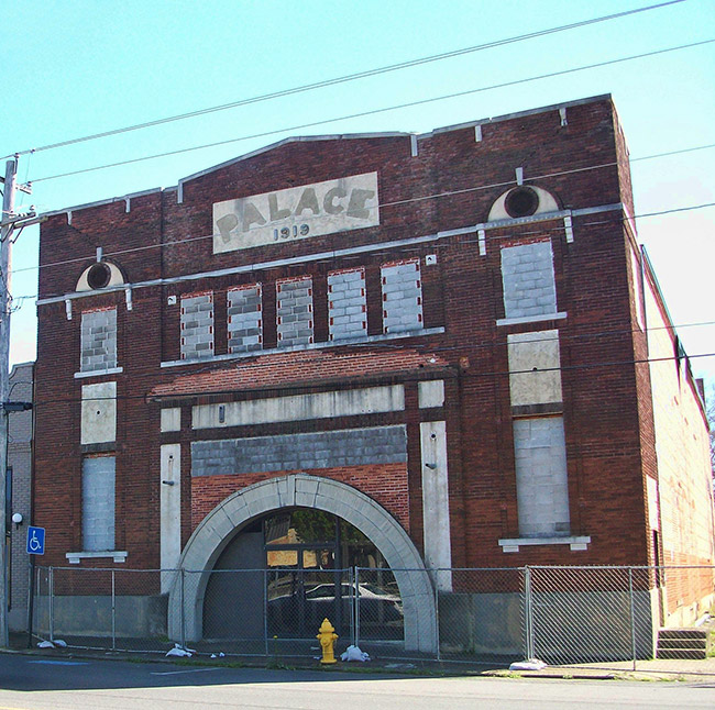 Multistory theater building with arched entrance behind chain link fence on street