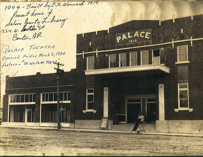 Multistory brick "Palace" theater and single-story buildings on street with handwritten notes