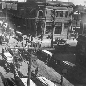White men and wagons filled with cotton on city street with multistory storefronts
