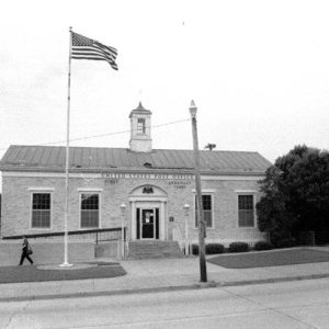 Single-story building with cupola on its roof and flagpole in front yard next to parking lot