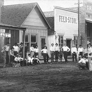 Group of white men in hats on dirt road with storefronts