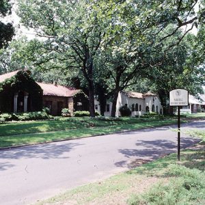 Brick house with ivy and white stucco house on street with trees and sign