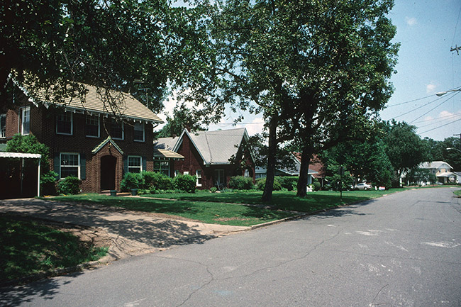 Two-story brick house and single-story brick house on street with trees in yard