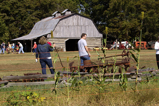 White crowd visiting farmstead with barn and machinery in field