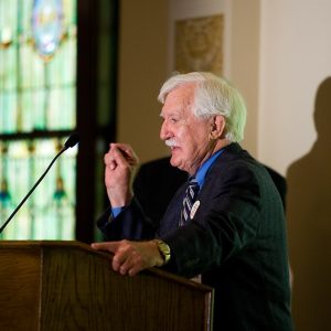 Old white man in suit speaking at a lectern