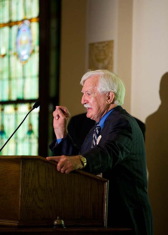Old white man in suit speaking at a lectern