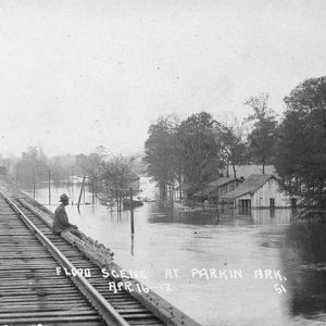 African-American man sitting on railroad bridge during a flood signed "Flood scene at Parkin April 16-17"
