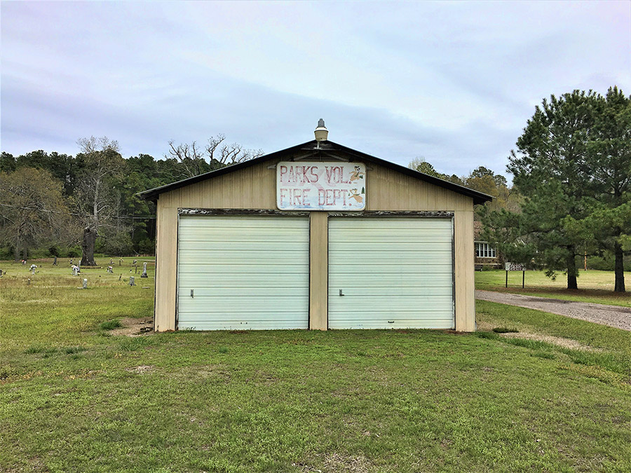 Metal two-car garage building with sign and cemetery on left side