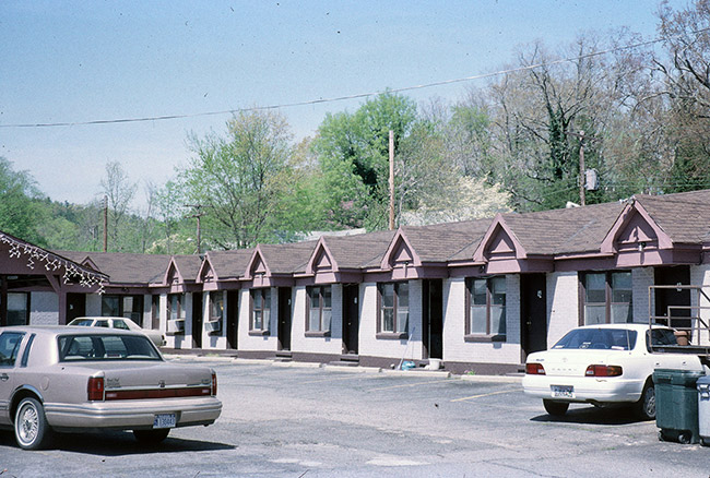Single-story motel building with identical apartments with pink trim and cars in parking lot