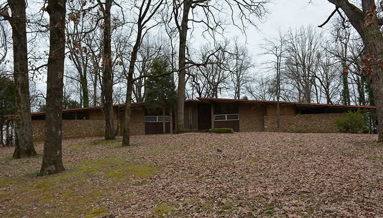 Brick house with angled flat roof on hill covered with fall leaves
