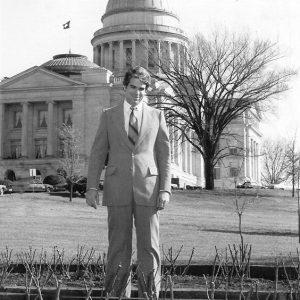 White man in suit standing outside large stone building with dome