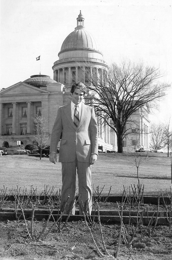 White man in suit standing outside large stone building with dome
