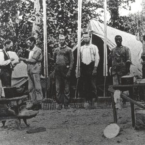 White men with rake like tools standing near tents and tables